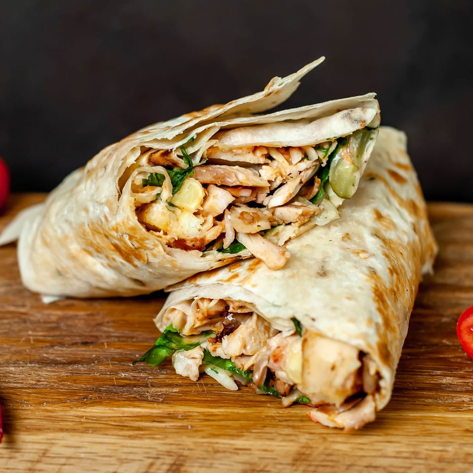 Two chicken shawarma wraps, cut in half, revealing meat and vegetables on a wooden board.
