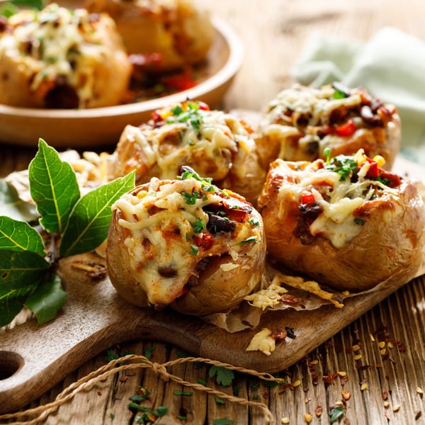 Four baked potatoes, stuffed with meat, vegetables, and melted cheese, on a wooden board.