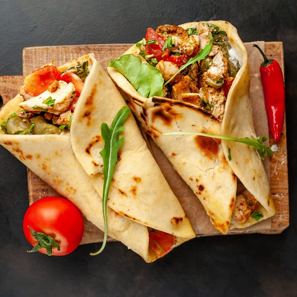 Two A1 Fusion Eats Midtown chicken wraps with tomatoes, arugula, and chili on a wooden board.