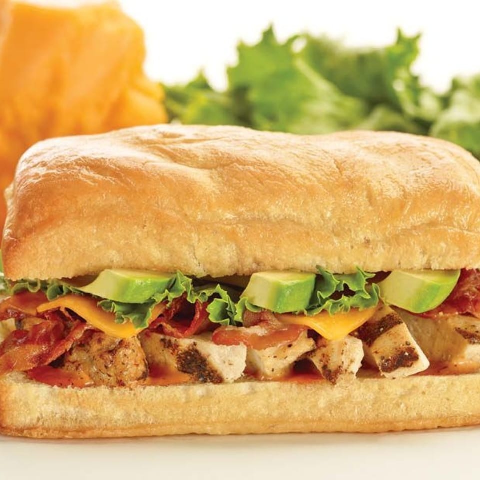 A A1 Fusion Eats Midtown chicken sandwich with bacon, avocado, cheese, and lettuce on a bun.